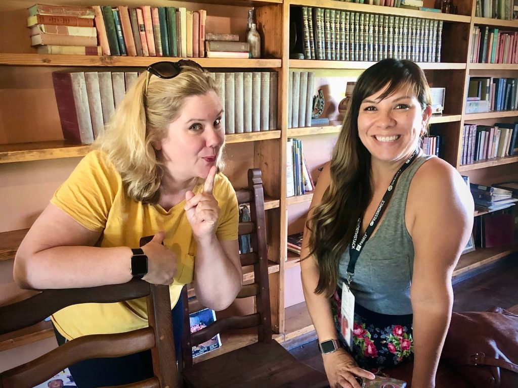 two women smiling while standing in front of a book shelf