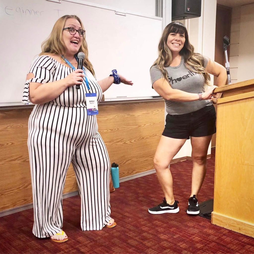 two women standing in front of a whiteboard and podium