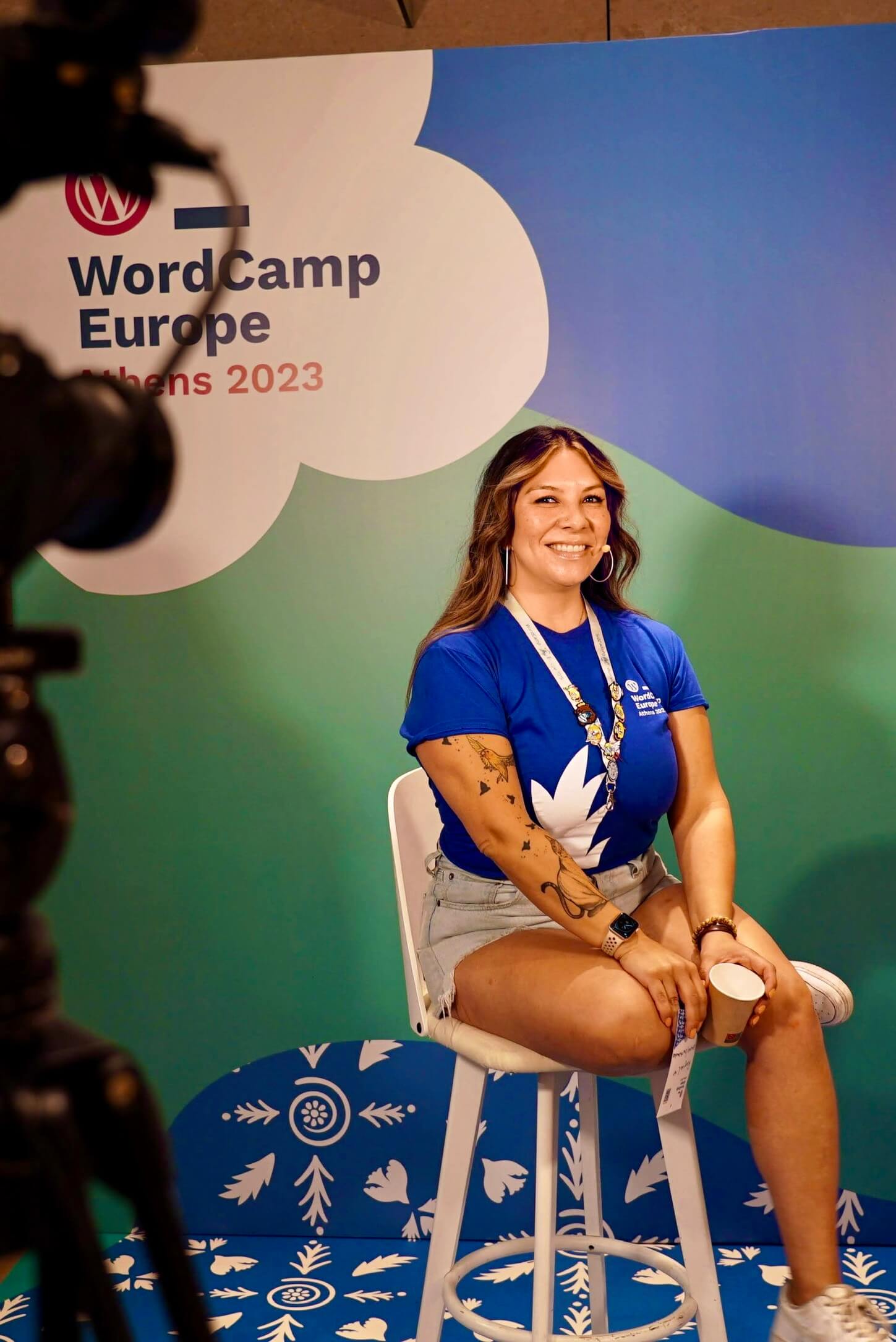 Raquel sitting on a stool in front of a camera with a head mic on